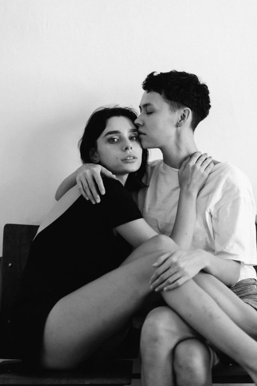 a black and white photo of two people sitting on a bench, a black and white photo, by Jessie Alexandra Dick, tumblr, antipodeans, non binary model, hug, two buddies sitting in a room, she looks like a mix of grimes
