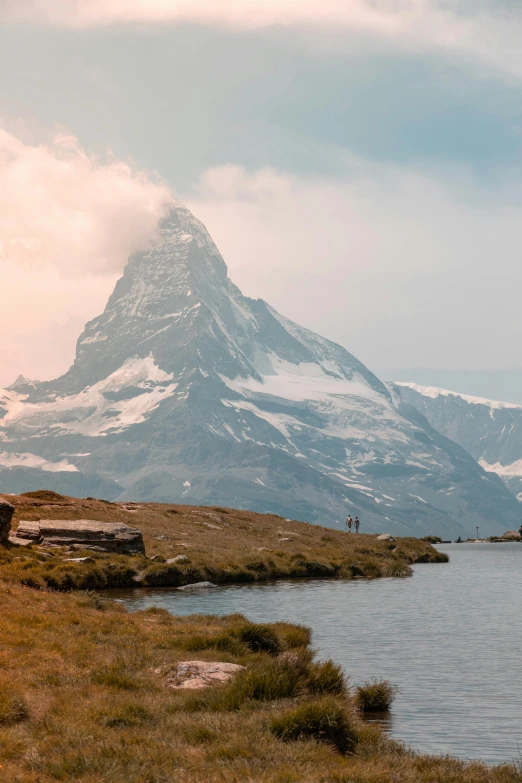 a mountain covered in snow next to a body of water, by Daniel Seghers, pexels contest winner, late summer evening, swiss modernizm, devils horns, 4 k cinematic panoramic view