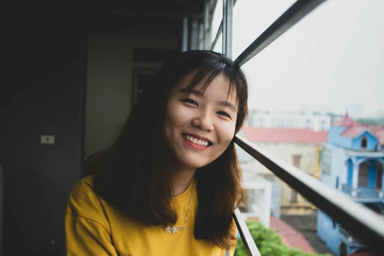a woman in a yellow shirt looking out a window, a picture, inspired by Ruth Jên, pexels contest winner, happening, smiling at camera, hoang long ly, profile image, student