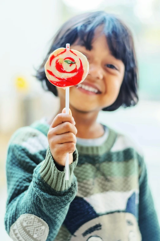 a little girl holding a lollipop in her hand, pexels contest winner, happily smiling at the camera, closeup at the food, square, boys