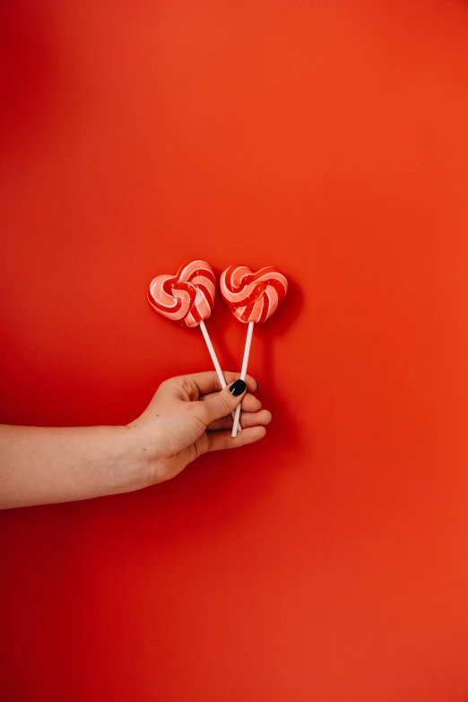 a person holding two lollipops in their hands, pexels contest winner, postminimalism, coral red, made of candy, red wall, recipe