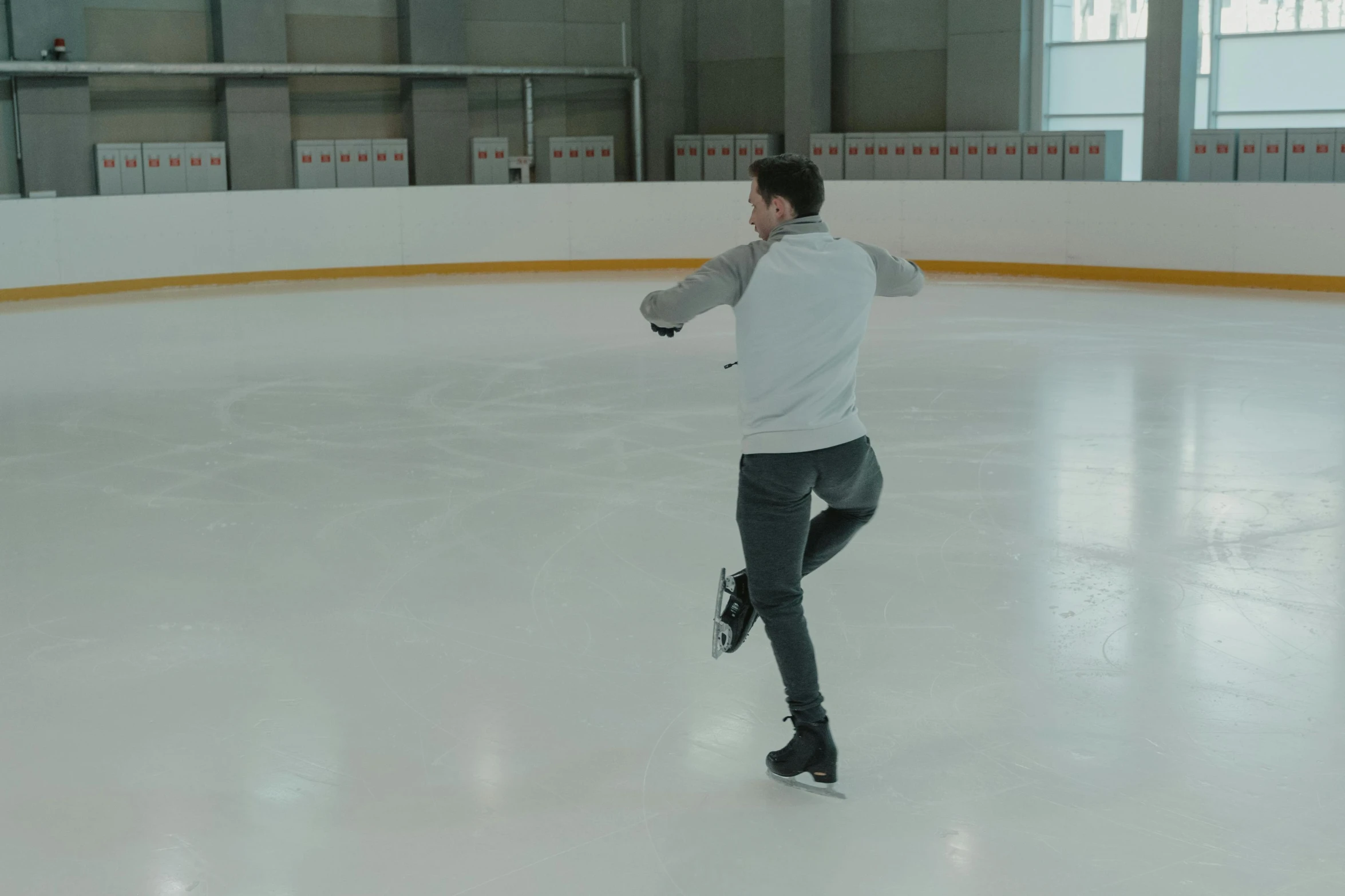 a man is skating on an ice rink, turned back to camera, the forefoot to make a v gesture, h3h3, grey