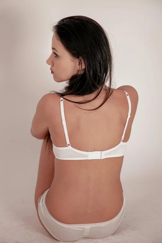 a woman in a white underwear sitting on a bed, showing her shoulder from back, bra strap, detailed product image, push-up underwire. intricate