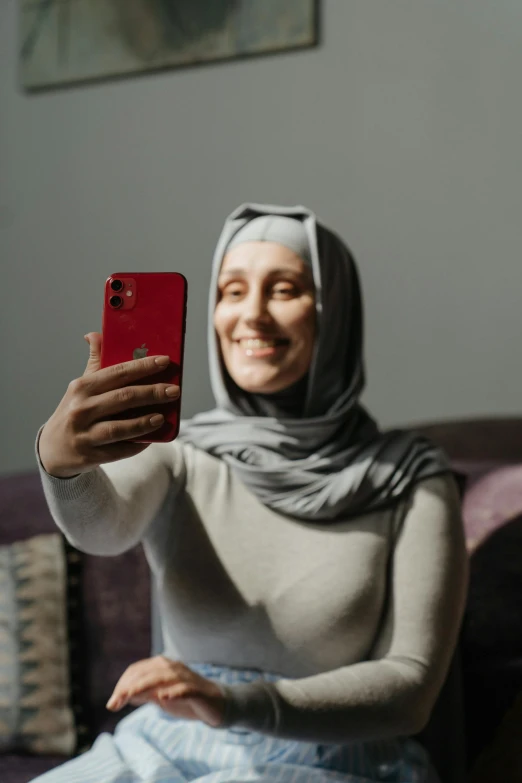 a woman sitting on a couch taking a picture of herself, a picture, inspired by Maryam Hashemi, pexels contest winner, hurufiyya, face covered, holds a smart phone in one hand, grey, trending on tiktok