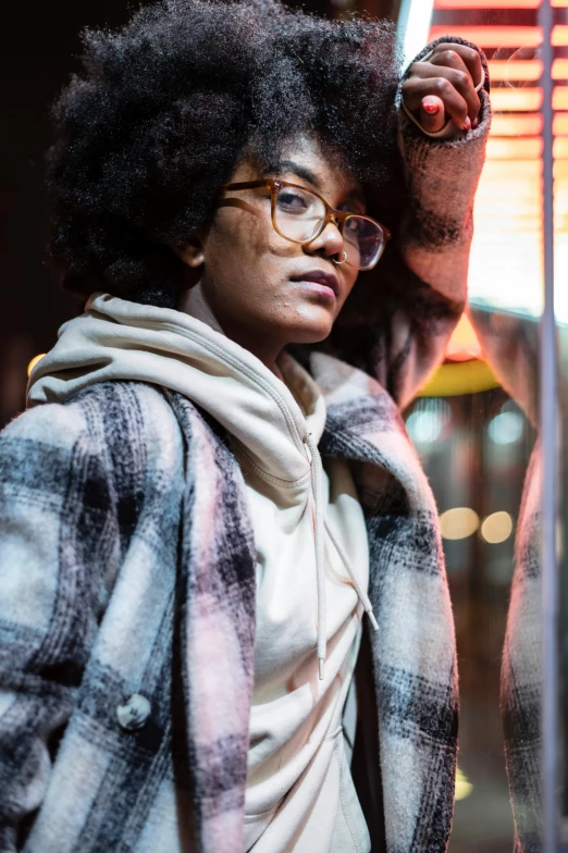 a woman with an afro standing in front of a window, by Jeffrey Smith, pexels, in square-rimmed glasses, black haired girl wearing hoodie, flannel, multiple lights