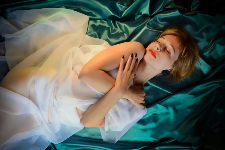 a woman in a white dress laying on a bed, inspired by Elsa Bleda, trending on pixabay, art photography, flowing teal-colored silk, on a velvet tablecloth, plastic skin, portait image