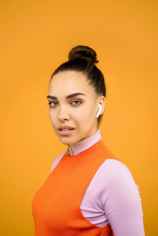 a woman standing in front of an orange background, trending on pexels, earbuds, gal gadot and tribbles, on grey background, topknot