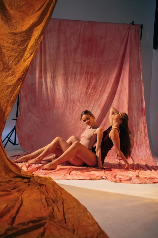 a couple of women sitting on top of a bed, by Elsa Bleda, gutai group, pink volumetric studio lighting, red ocher, loincloth, promo image