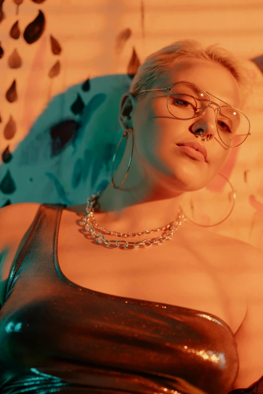 a woman wearing glasses laying on top of a bed, an album cover, inspired by Elsa Bleda, trending on pexels, holography, platinum blonde, bad bunny, wearing chains, portrait mode photo