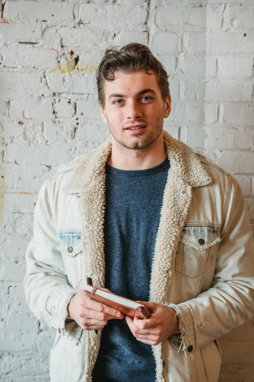 a man standing in front of a brick wall holding a cell phone, sydney sweeney, with slight stubble, studious, xqc