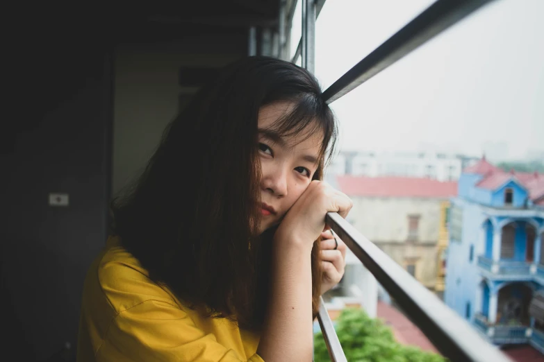 a woman in a yellow shirt looking out a window, by Tan Ting-pho, pexels contest winner, realism, 🤤 girl portrait, pale round face, student, dang my linh