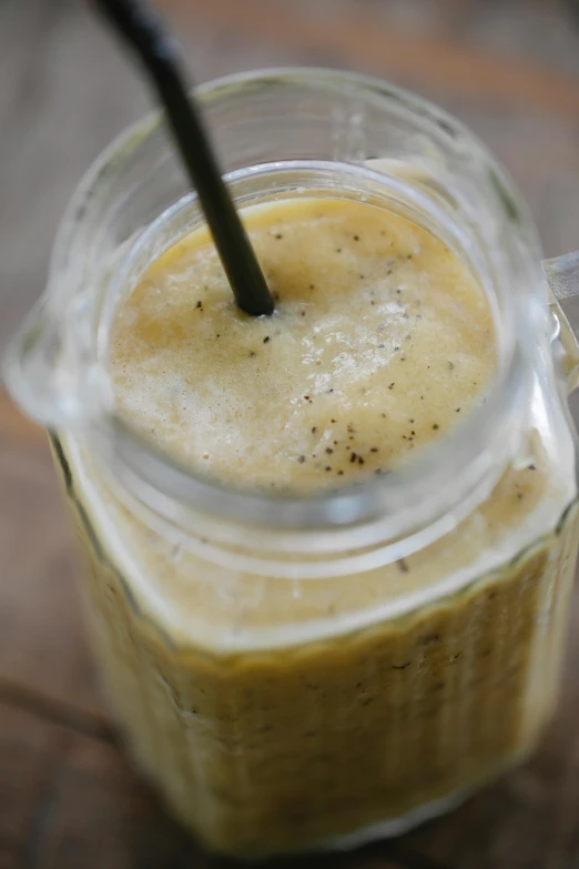 a glass filled with liquid sitting on top of a wooden table, vanilla smoothie explosion, grain”