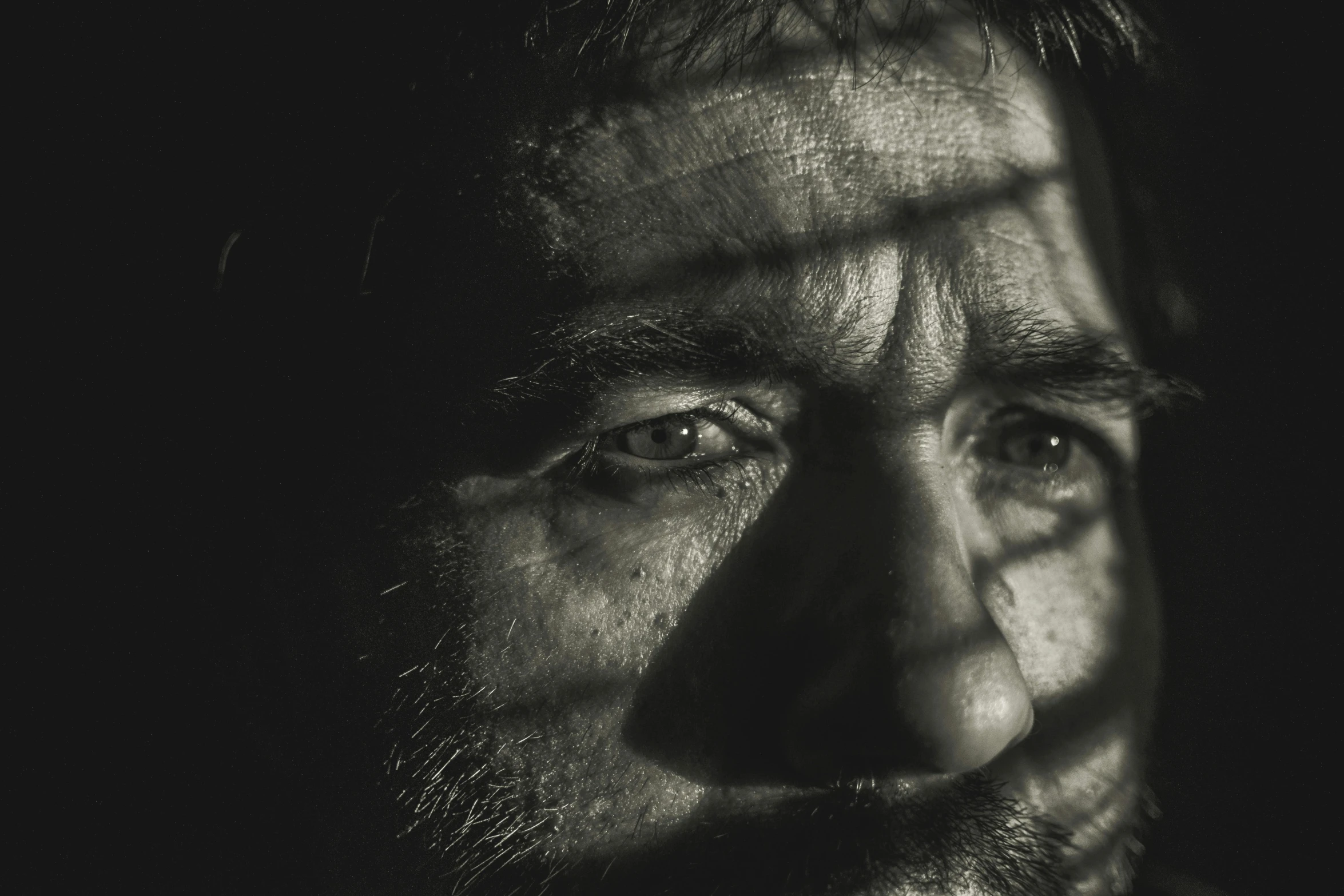 a black and white photo of a man with a beard, pexels contest winner, photorealism, faces covered in shadows, sad eyes, face is brightly lit, promo image