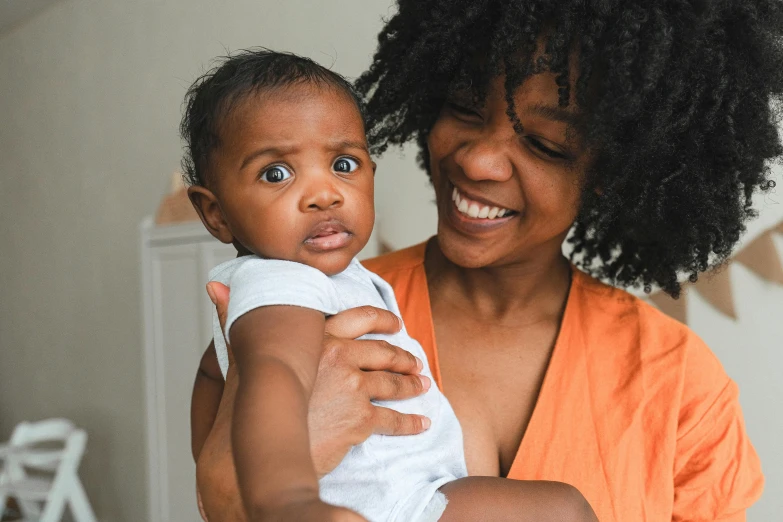 a woman holding a baby in her arms, by Carey Morris, pexels contest winner, with brown skin, thumbnail, mischievous look, rectangle