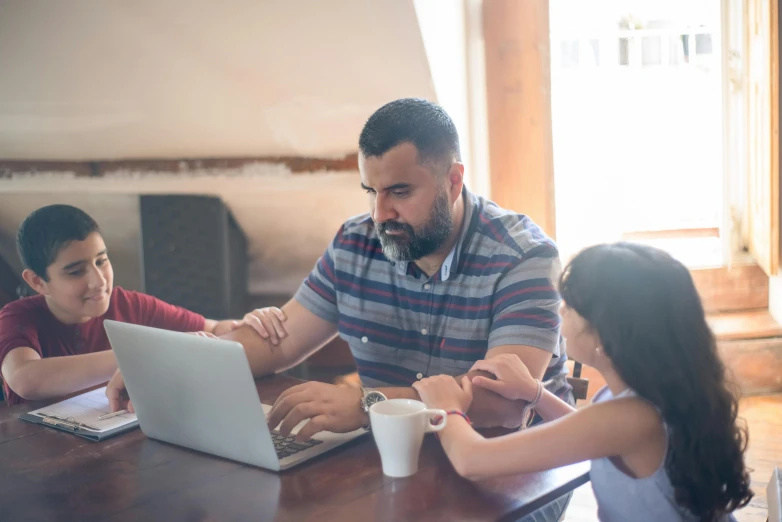 a group of people sitting around a table with a laptop, profile image, husband wife and son, multiple stories, teaching