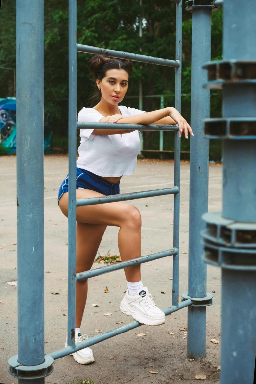 a woman leaning on a metal bar in a park, an album cover, unsplash, arabesque, wearing white sneakers, portrait of kim kardashian, blue shorts, 15081959 21121991 01012000 4k