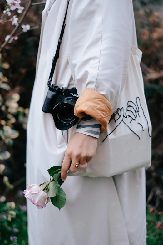 a woman holding a camera and a flower, by Lucia Peka, unsplash, pouches, wearing white clothes, outlined hand drawn, photo of a rose