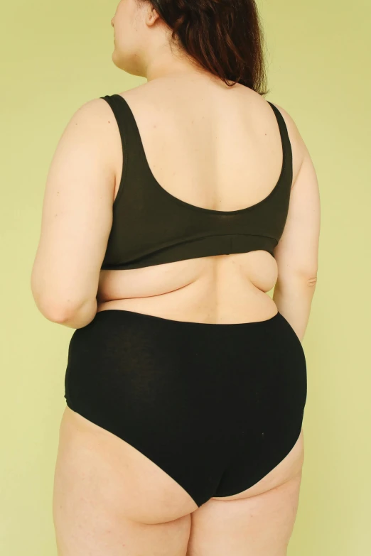 a woman in black underwear standing in front of a green wall, by Ren Hang, unsplash, morbidly obese, back view », cut out, failed cosmetic surgery