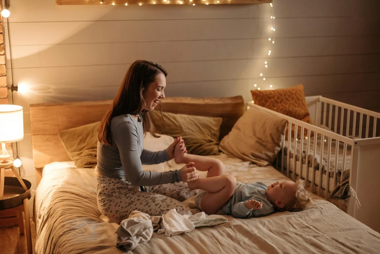 a woman sitting on top of a bed next to a baby, pexels contest winner, warm lights, having a good time, manuka, fully functional