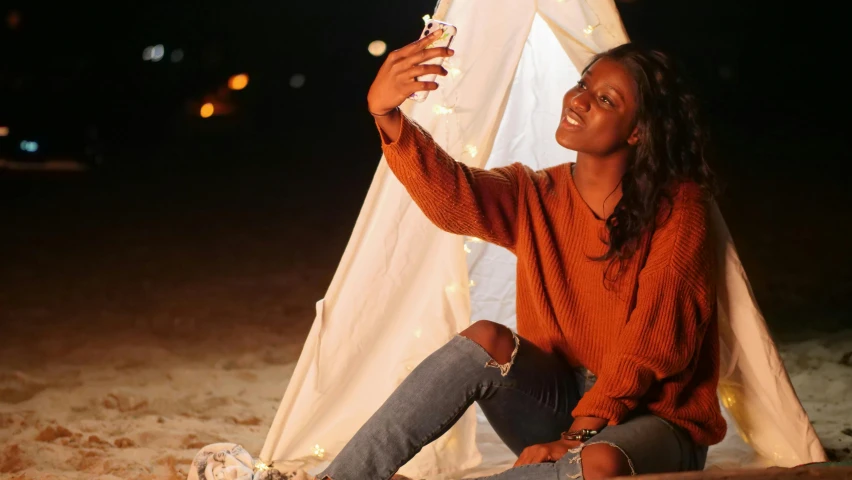 a woman sitting on top of a sandy beach next to a tent, a portrait, pexels contest winner, happening, holding up a night lamp, in love selfie, brown skin, profile image