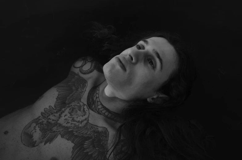 a black and white photo of a man with tattoos, by Jessie Alexandra Dick, conceptual art, long flowing hair underwater, laying down, androgynous vampire, uploaded