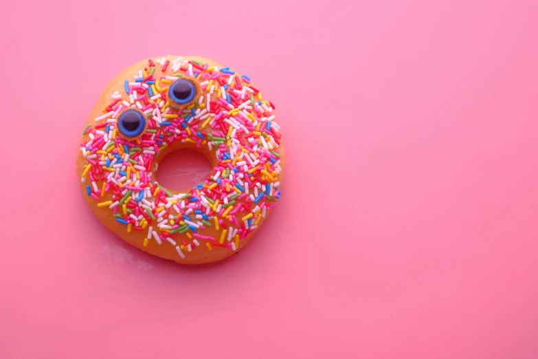 a donut with sprinkles on a pink surface, by Niko Henrichon, pexels, pointed teeth and several eyes, animal - shaped bread, 15081959 21121991 01012000 4k