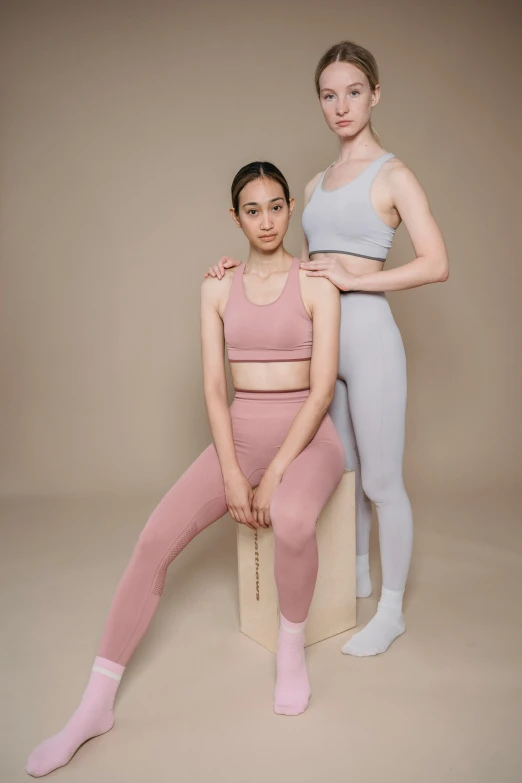 a couple of women sitting next to each other, standing athletic pose, muted colours, photoshoot for skincare brand, basia tran