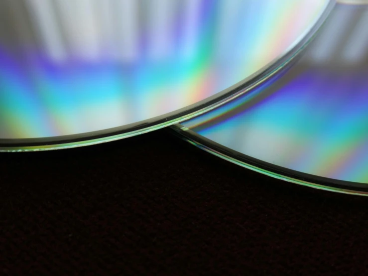 a couple of cds sitting on top of a table, by Jan Rustem, pexels, computer art, highly detailed refraction, bottom body close up, thin glowing devices, bluray