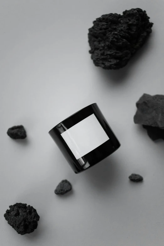 a candle sitting on top of a table next to rocks, a black and white photo, shungite bangle, square black pupil centered, black color on white background, product advertisement