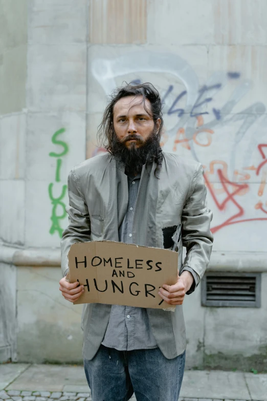 a man standing on a sidewalk holding a sign, by Matija Jama, renaissance, hunger, scruffy looking, promo image, gettyimages