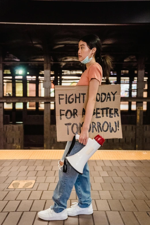 a woman holding a sign that says fight day for better tomorrow, by Julia Pishtar, unsplash contest winner, jamel shabazz, young asian woman, 🚿🗝📝