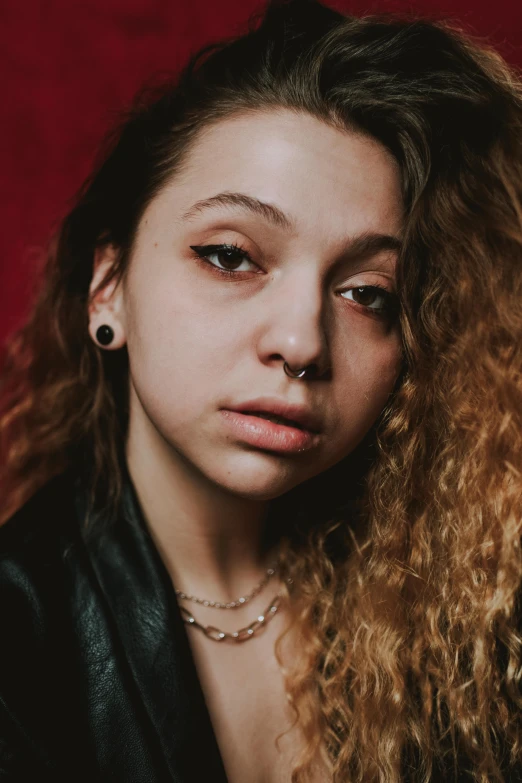 a woman with long curly hair posing for a picture, inspired by Elsa Bleda, antipodeans, chrome facial piercings, looking sad, high resolution image, evenly lit