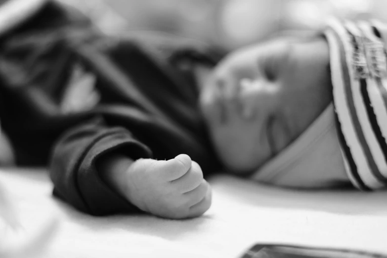 a baby laying on top of a bed next to a cell phone, a black and white photo, by Caroline Mytinger, pexels, symbolism, in hospital bed, profile image, diverse, finger