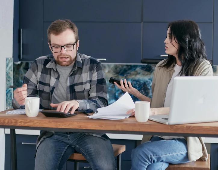 a man and a woman sitting at a kitchen table, working hard, worried, realistic »