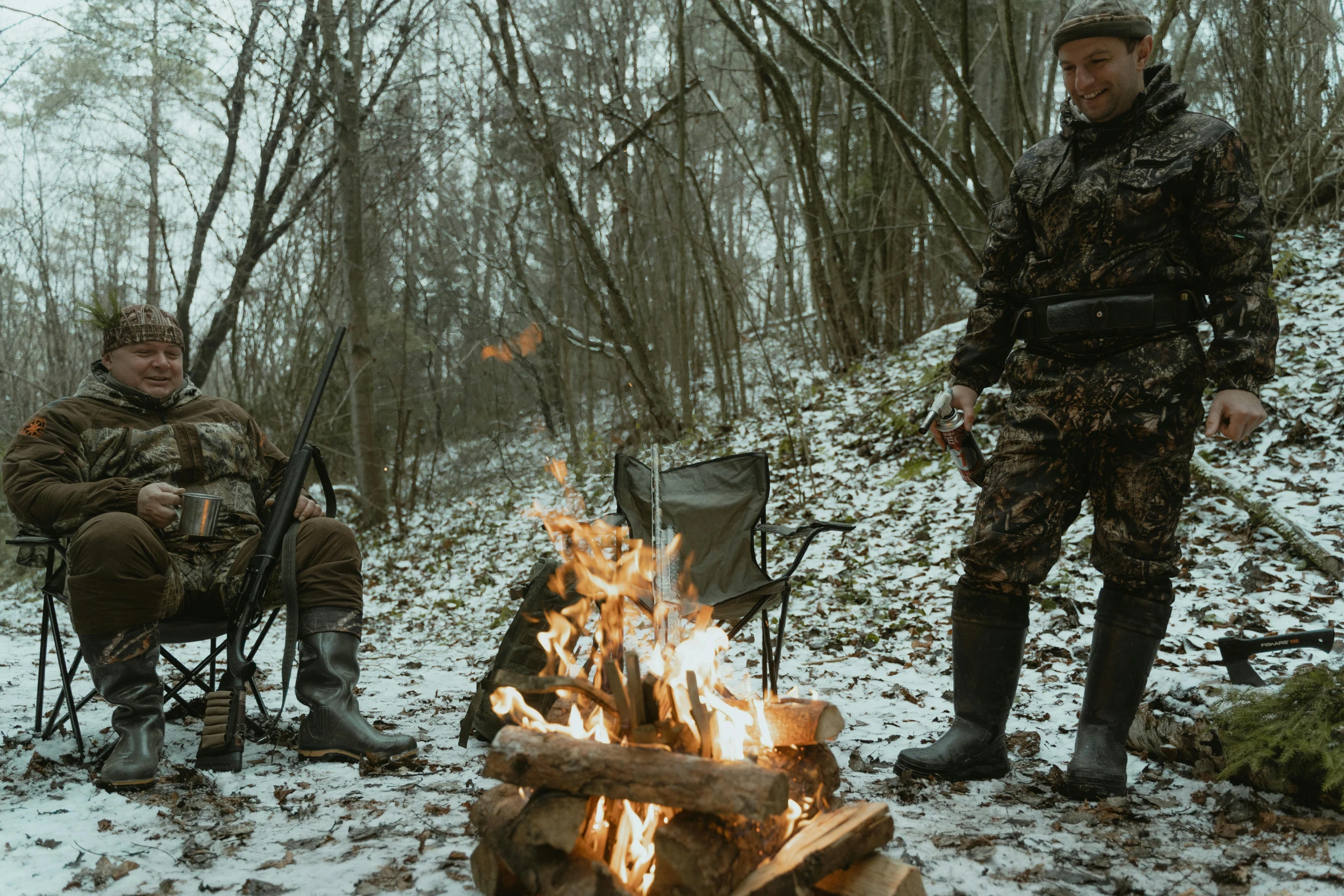 two men sitting around a campfire in the woods, by Emma Andijewska, hunters gear, wearing camo, winter setting, thumbnail