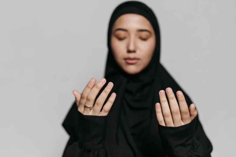 a woman in a black hijab is praying, inspired by Modest Urgell, trending on pexels, hurufiyya, shrugging, partially cupping her hands, asian human, brown