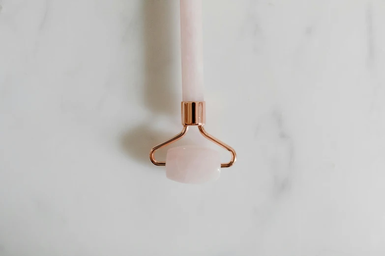 a rose quartz stone roller on a marble surface, by Emma Andijewska, fork, holding a candle holder, extended clip, looking straight to camera