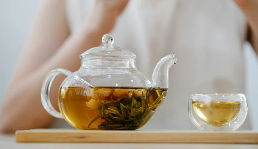 a person sitting at a table with a cup of tea and a teapot, inspired by Cui Bai, trending on pexels, with clear glass, jasmine, white, jar on a shelf