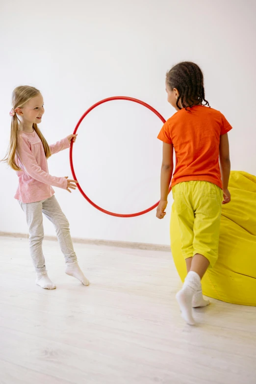 two little girls playing with a hula hoop, by Nina Hamnett, wearing red and yellow clothes, activity play centre, holding a balloon, on grey background
