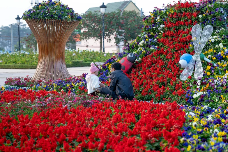 a couple of people sitting on top of a bed of flowers, interactive art, in red gardens, dubai, bouquets, multicoloured