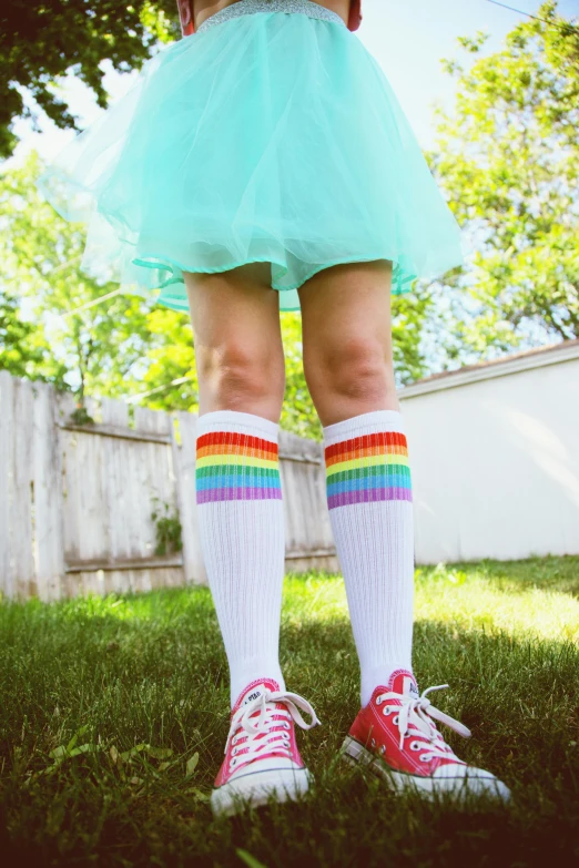 a woman standing on top of a lush green field, striped socks, rainbow accents, on sidewalk, girl standing