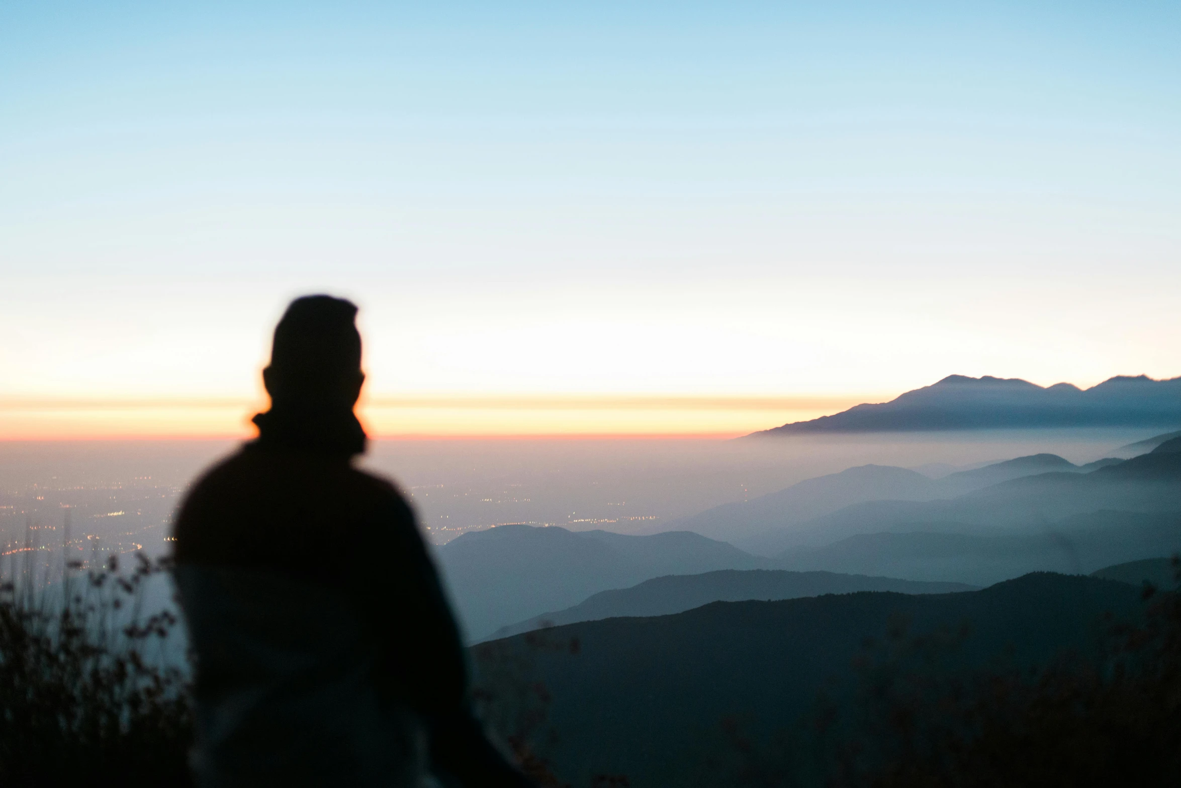 a person standing on top of a mountain at sunset, by Niko Henrichon, unsplash contest winner, blurry distant background, profile image, japan mountains, profile view perspective