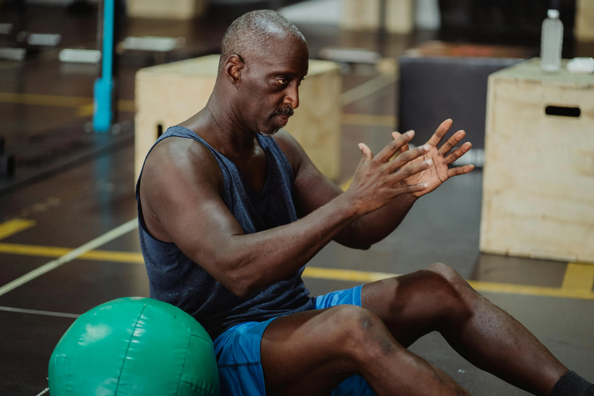 a man sitting on top of a green ball, local gym, man is with black skin, his palms are sweaty, profile image