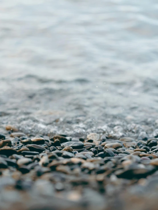 a pile of rocks sitting on top of a beach, body of water, upclose, wet feet in water, unsplash 4k