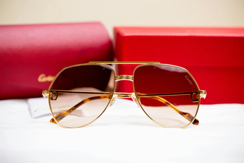 a pair of sunglasses sitting next to a red box, by Julia Pishtar, gold layers, charles, caramel, thumbnail