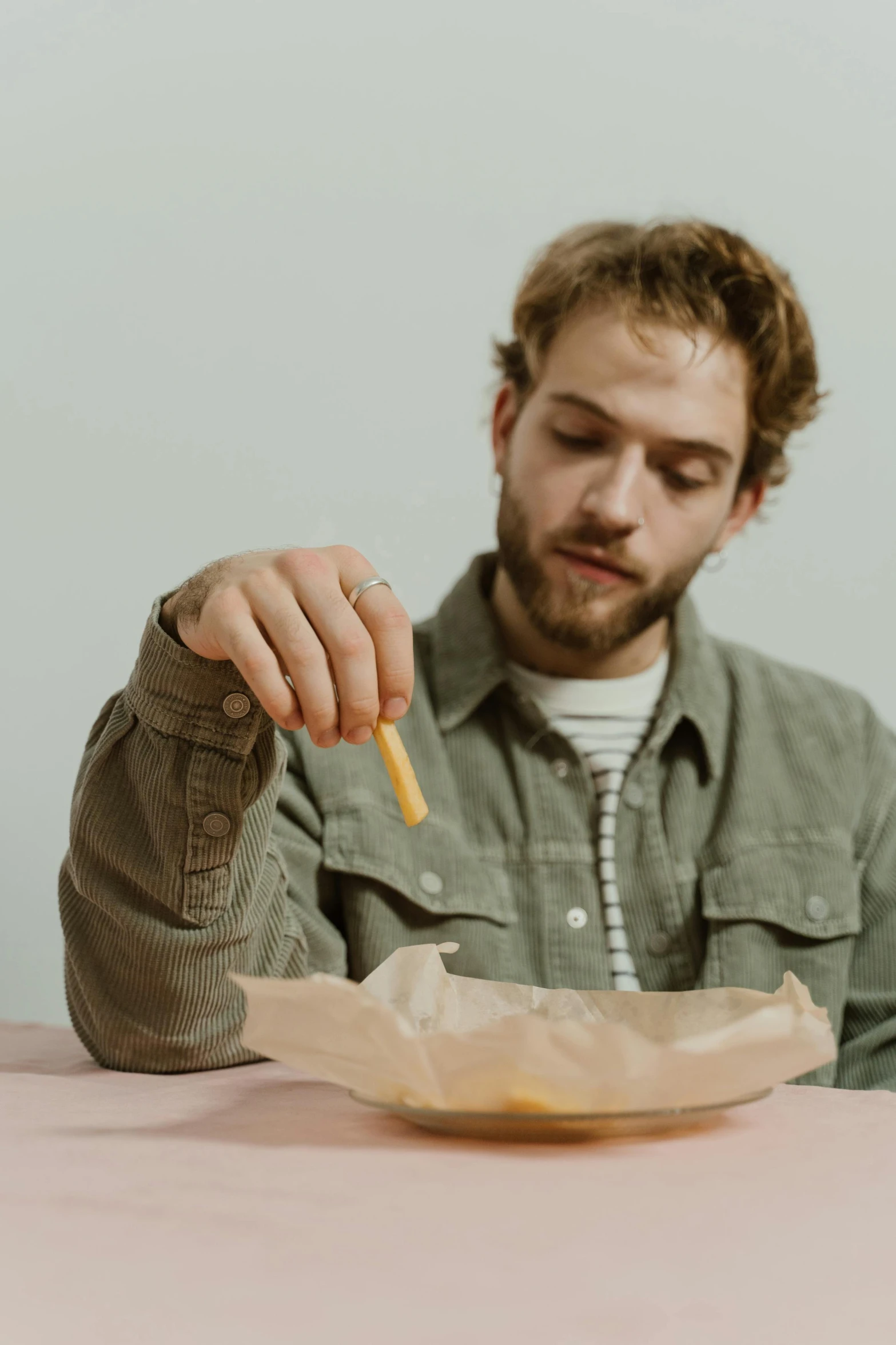 a man sitting at a table with a bowl of food, an album cover, trending on pexels, holding wand, zachary corzine, golden ration, on a pale background