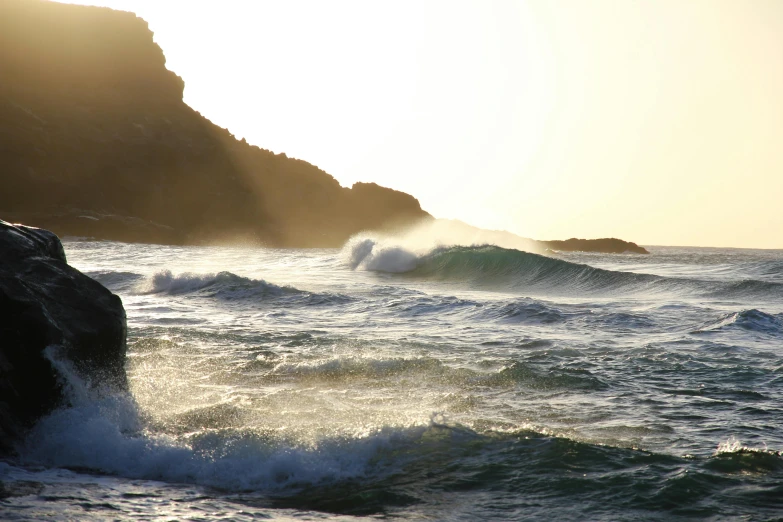 a person riding a surfboard on a wave in the ocean, golden hour photograph, cornwall, cliffs, nature photo