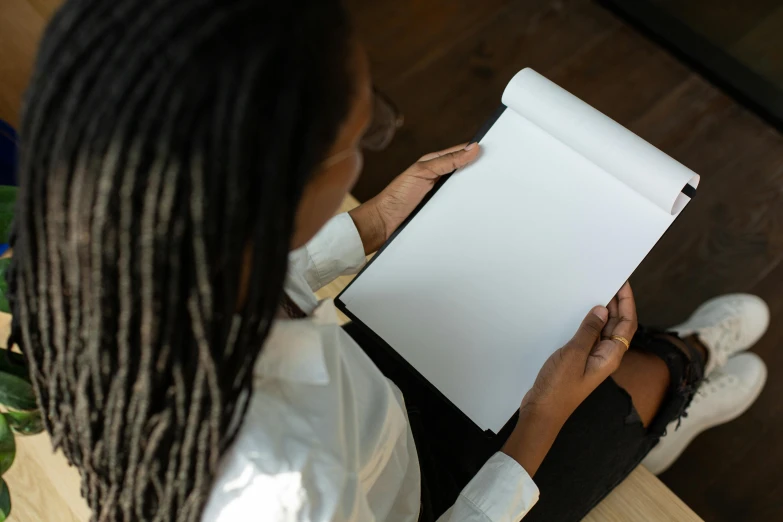 a woman sitting on the floor holding a piece of paper, a drawing, by Carey Morris, pexels contest winner, black female, holding a clipboard, pictured from the shoulders up, with a sleek spoiler