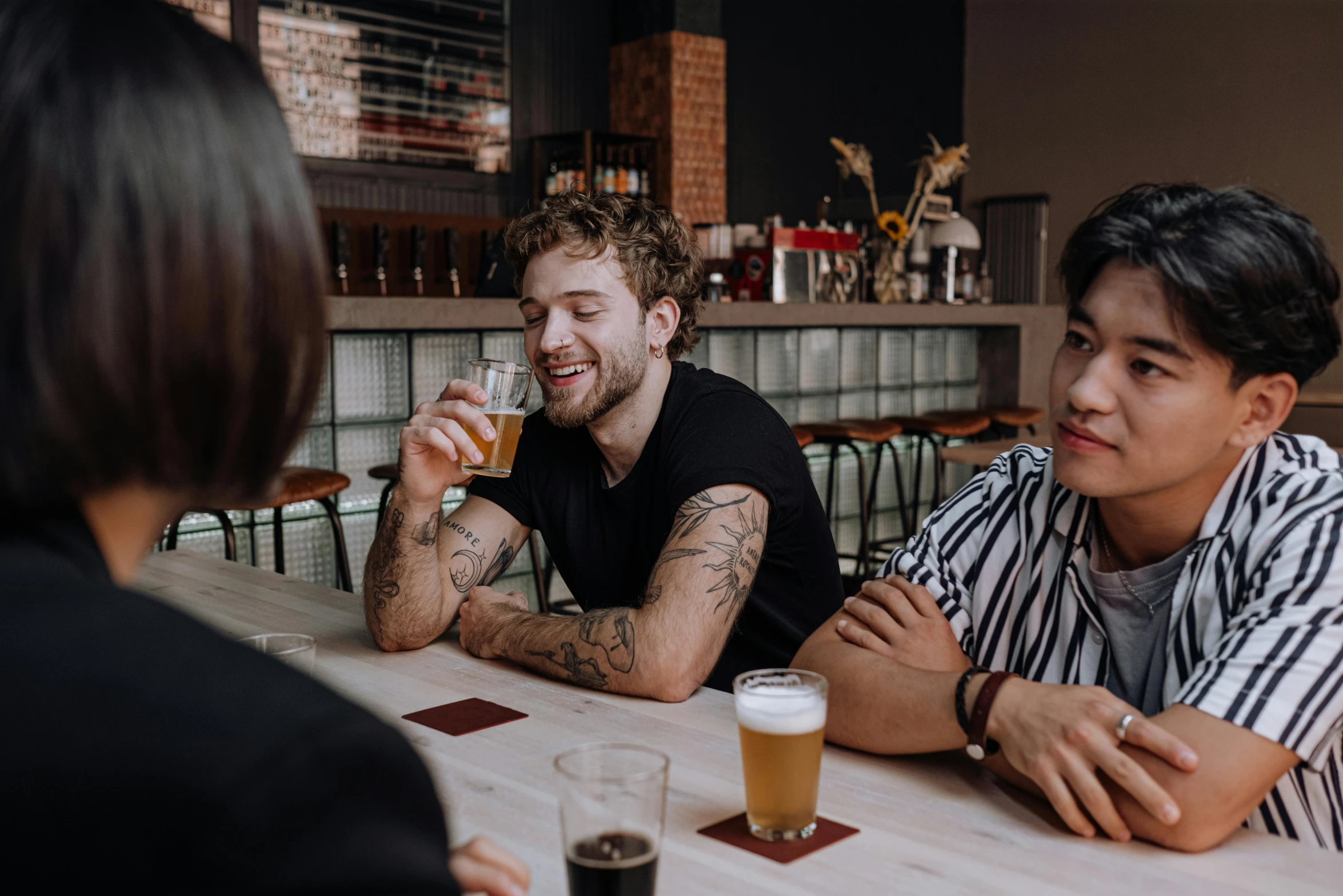 a group of people sitting around a wooden table, by Adam Marczyński, pexels contest winner, a pint of beer sitting on a bar, tyler edlin and natasha tan, flirting smiling, aussie baristas