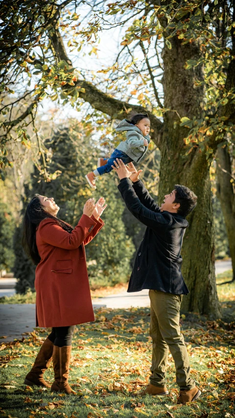 a man and woman playing with a child in a park, a picture, by Alison Debenham, pexels, leaping from babaob tree, square, autum, high quality photo